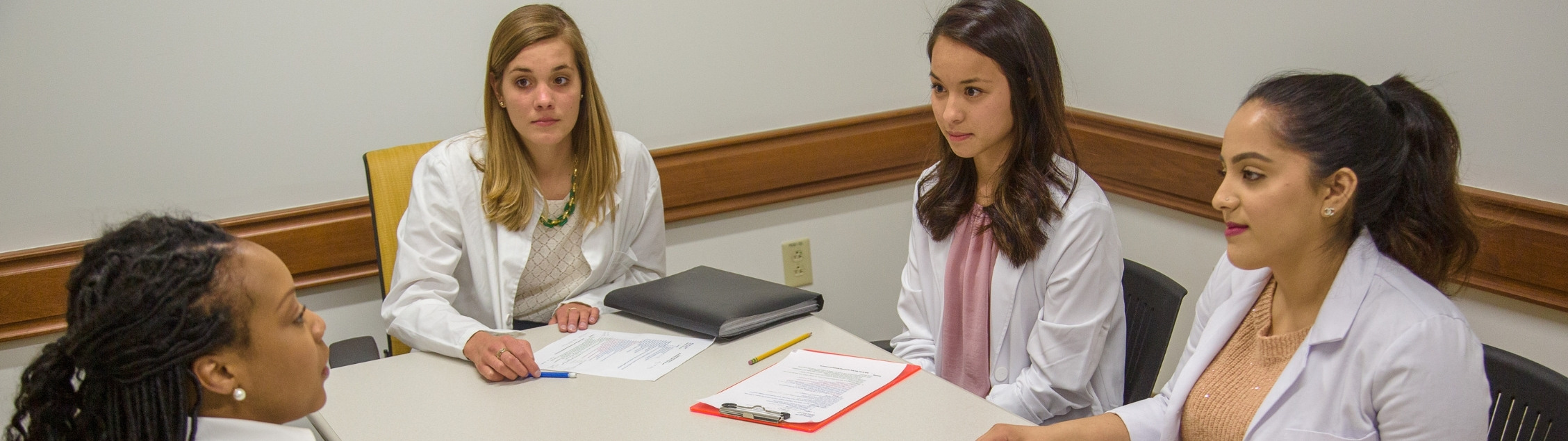 Students in white coats sit at interview table