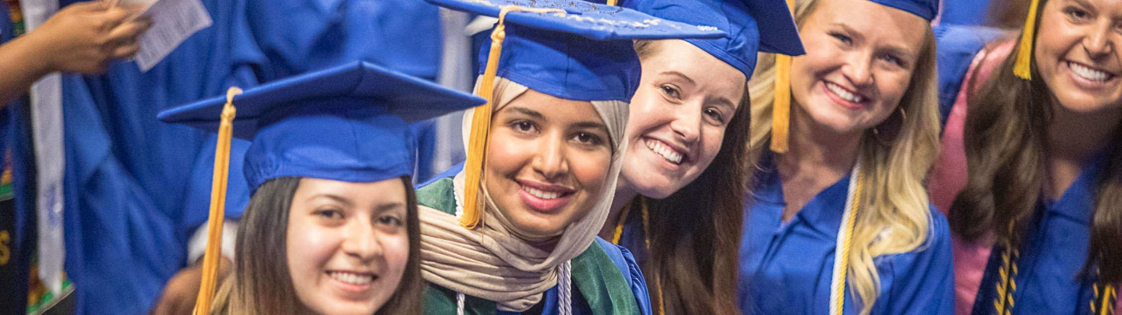 Students in blue gowns pose together at graduation